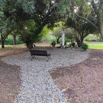 Un parque con un sendero de grava, una banca y una estatua.
