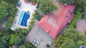 An aerial view of a property with a swimming pool, a red-roofed building, and surrounding greenery. - Arizona Ranch Hotel (Girardot)