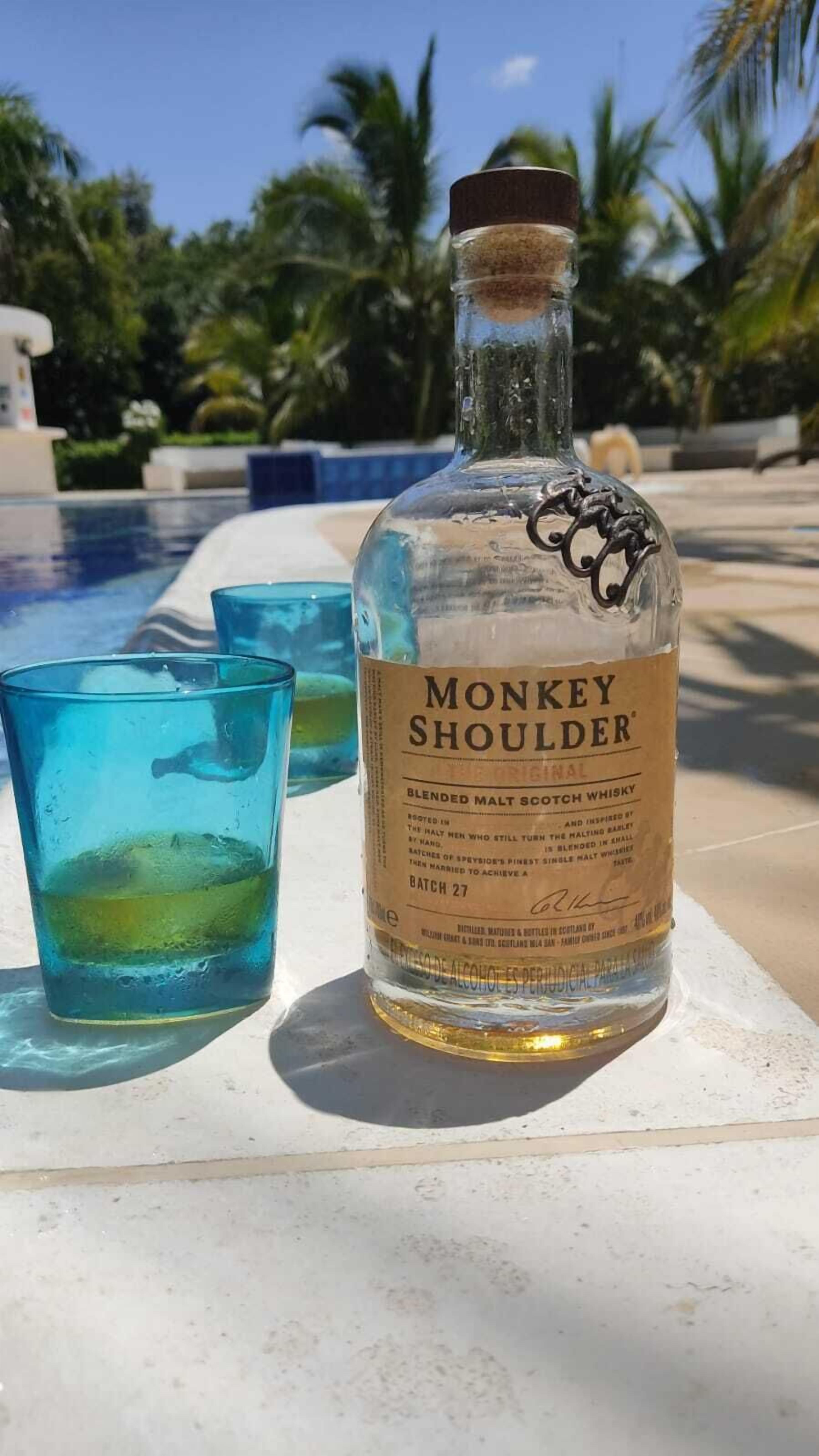 Une bouteille de whisky Monkey Shoulder et deux verres sur une table au bord de la piscine.