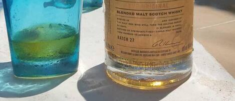 A bottle of Monkey Shoulder whisky and two glasses on a poolside table.