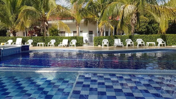 A swimming pool with checkered tiles, surrounded by white lounge chairs and palm trees. - Arizona Ranch Hotel (Girardot)