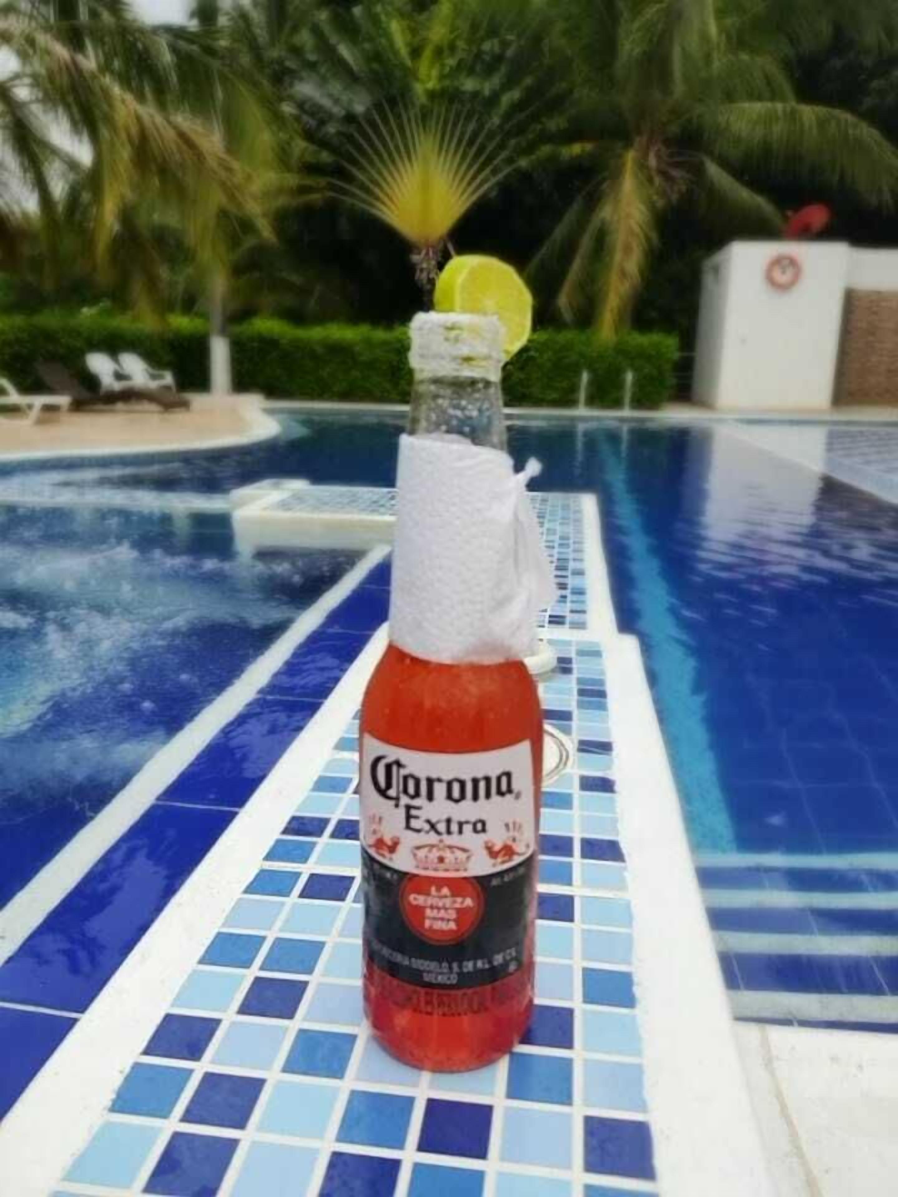 A bottle of Corona Extra beer on a poolside with a tropical background.