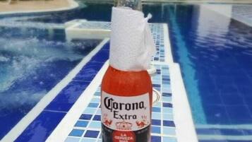 A bottle of Corona Extra beer on a poolside with a tropical background.