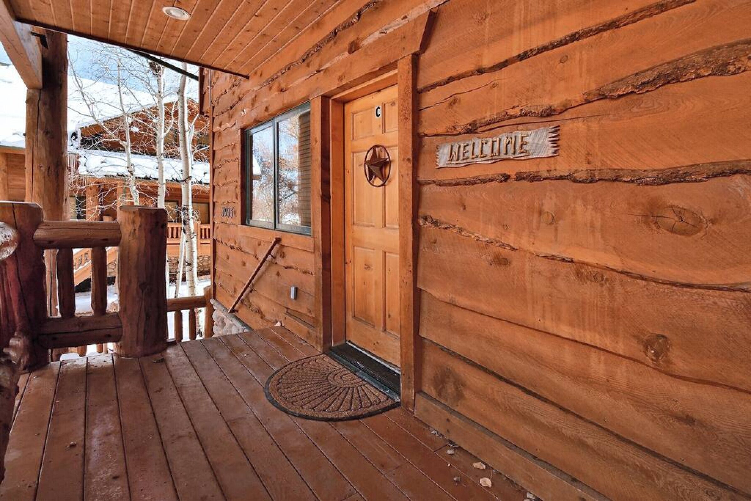 A wooden cabin with a wooden door marked "MELTINE," a window, and a porch with a bench.