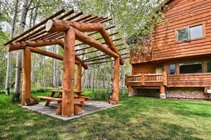 Eine Holzhütte mit Steinunterbau, einer Holzdiele und einem Picknicktisch inmitten eines bewaldeten Gebiets.