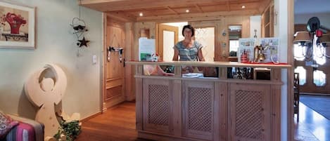 Un espace d’accueil avec un comptoir en bois, une personne derrière le comptoir et une porte donnant sur une autre pièce.