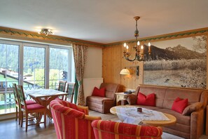 A cozy room with a dining table, chairs, a sofa, and a large window with a view of a mountainous landscape. - No. 8 Fewo Panoramablick - Gästehaus Braito (Grän)