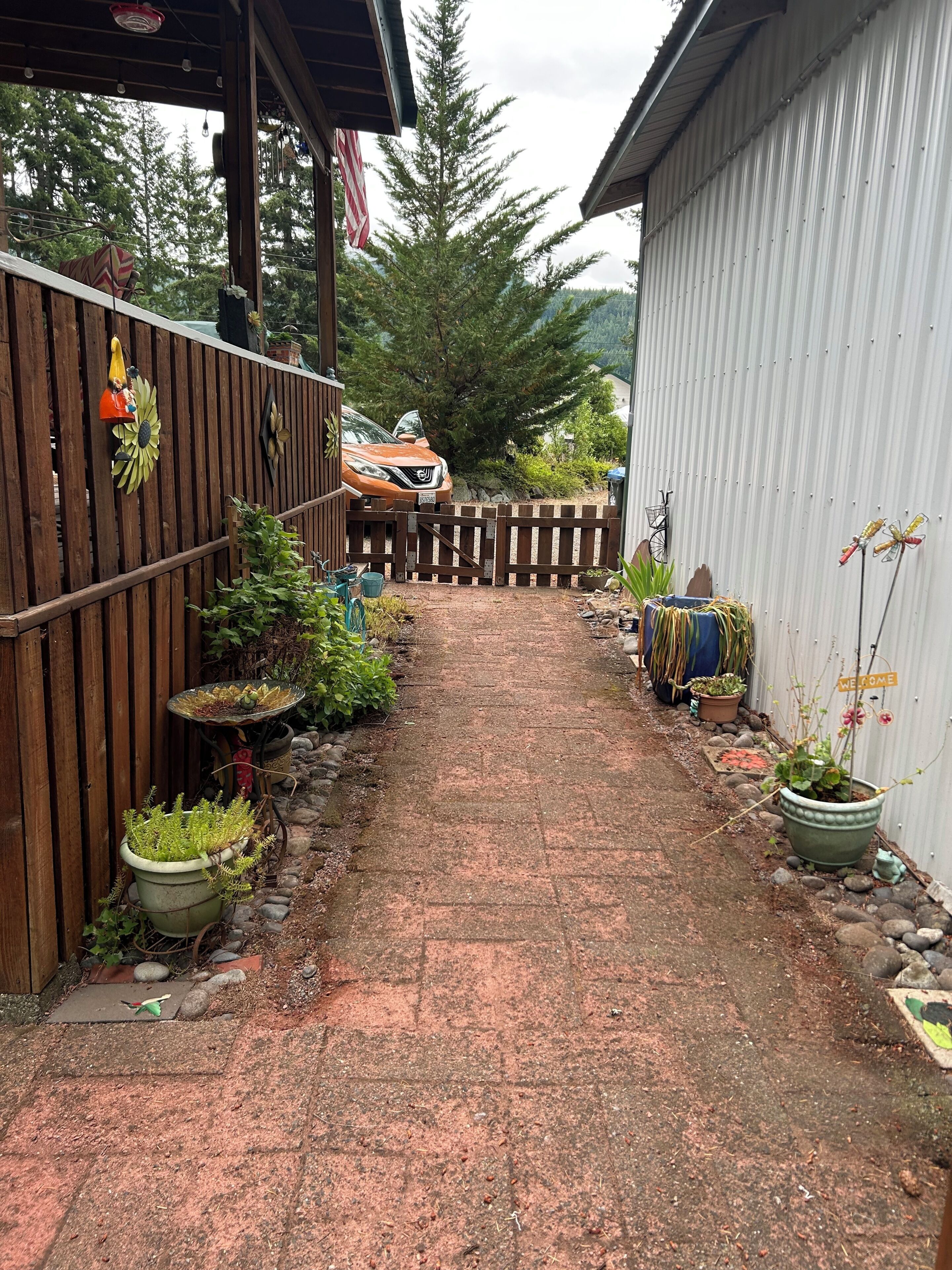 A paved pathway leading to a vehicle, flanked by wooden fences and potted plants.