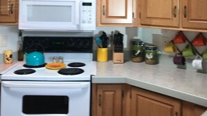 Una cocina con armarios de madera, microondas blanco, estufa y tetera azul verdoso.
