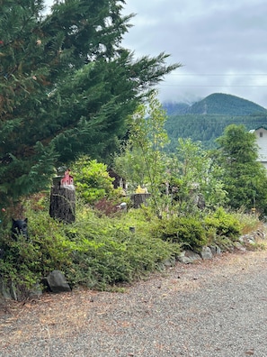 Un sendero de grava serpentea a través de un jardín con follaje exuberante y un pequeño comedero para pájaros.