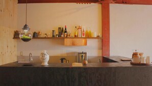 Una cocina con encimera de madera, lámpara colgante, estante con botellas y cafetera.