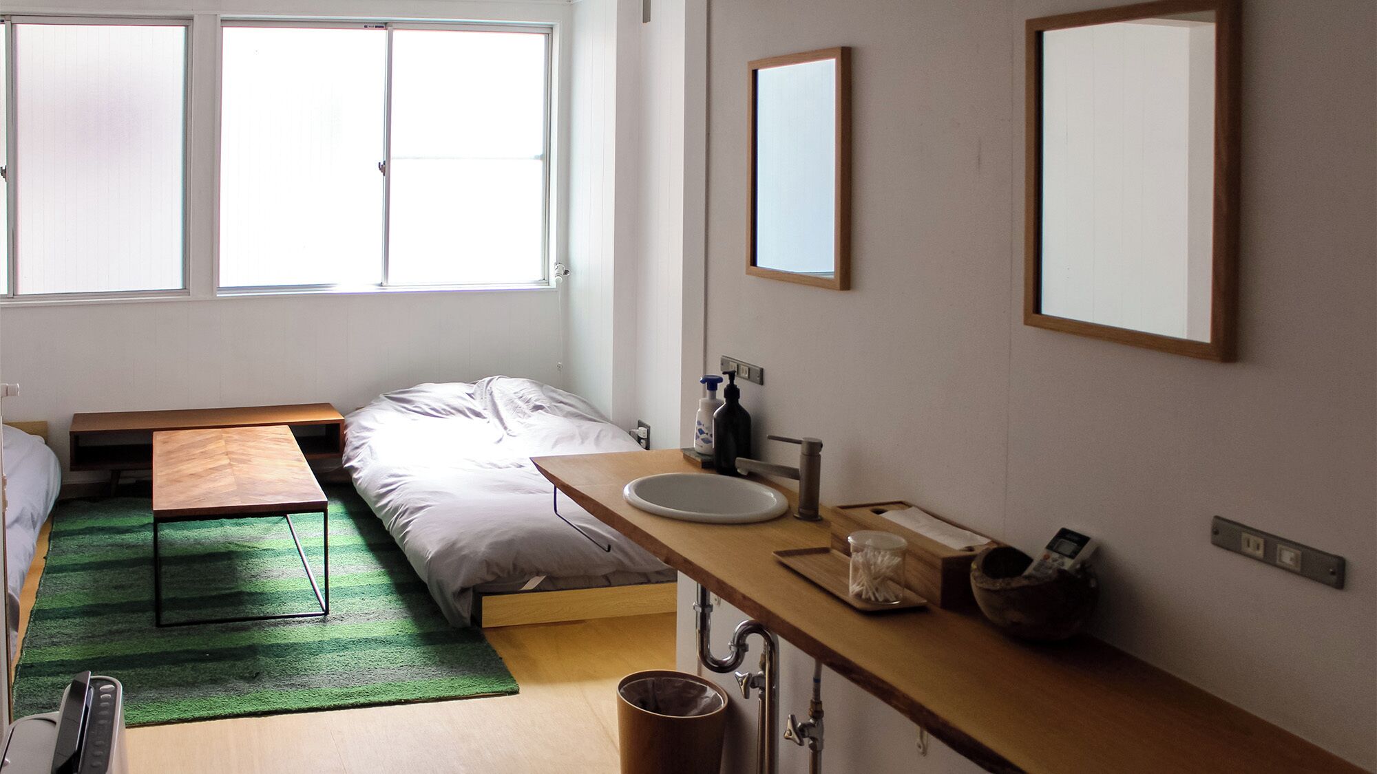 A compact room with a bed, a small table, a sink, and a mirror.