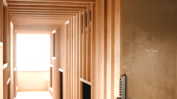 Un pasillo con una puerta identificada como “Habitación de Huéspedes 101-219” que conduce a una habitación luminosa.