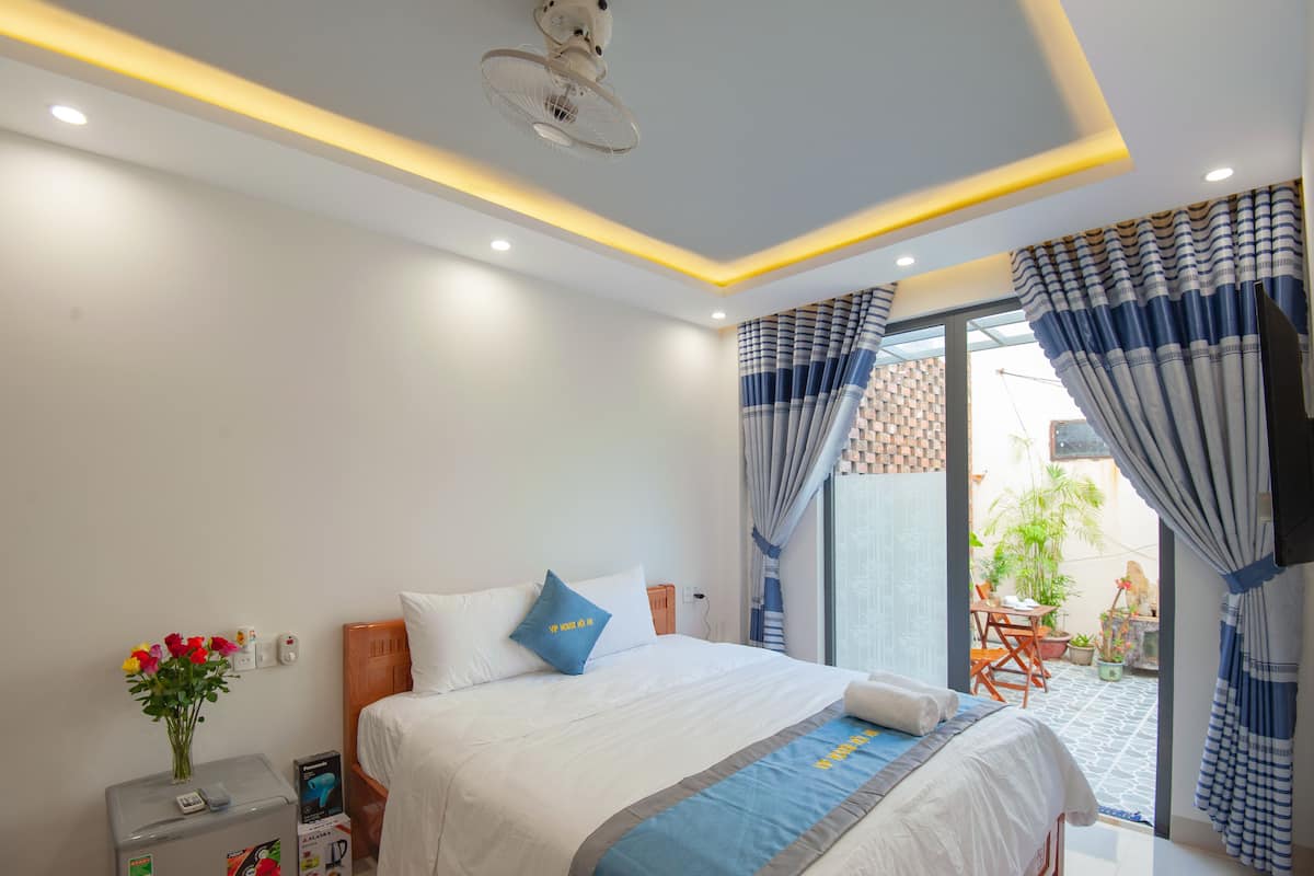 A hotel room with a bed, bedside table, and a small balcony with plants.