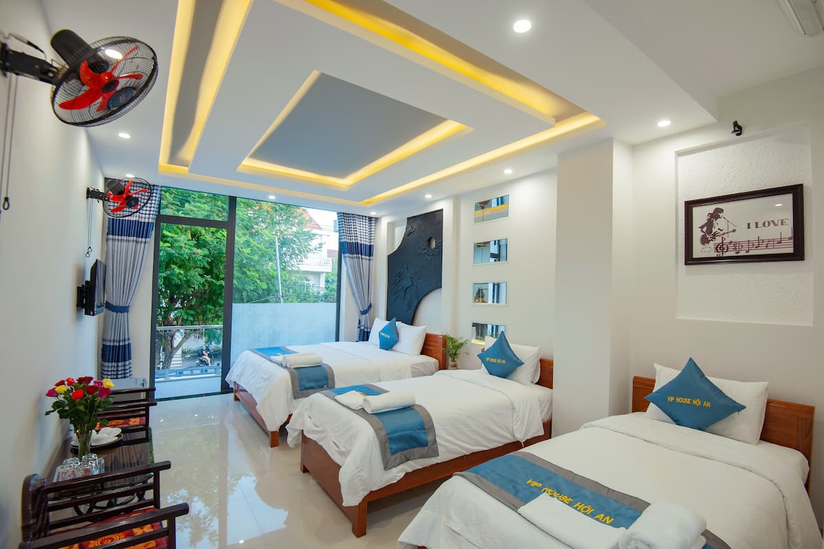 A hotel room with two beds, a dining area, and a view of greenery outside.