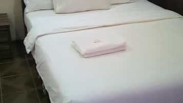 A neatly made bed with white bedding and pillows, a small bedside table, and a wall-mounted picture.