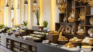 A buffet setup with various food items, including bread, pastries, and salads, arranged on a counter with overhead lighting. - Florida Hotel (Nha Trang)