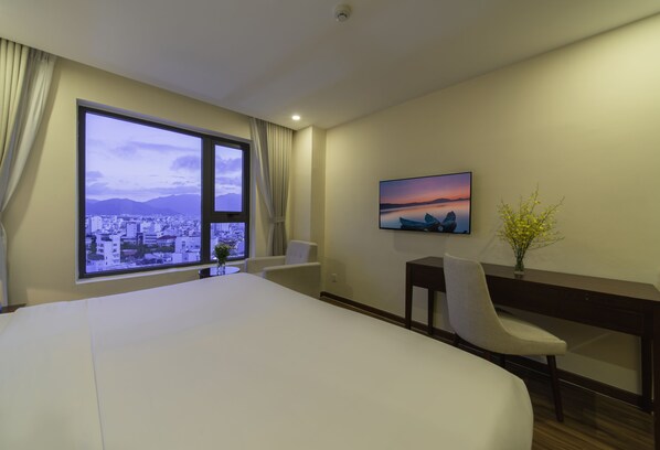 Habitación de hotel con una cama grande, un escritorio, una silla, un televisor y una ventana con vista a la ciudad.