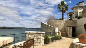 A stone pathway leading to a building with a view of the water and hills. - Lake front condo at the Island (Lago Vista)