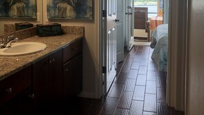 A bathroom with a sink, mirror, and artwork. A hallway leads to a bedroom with a view of the outdoors. - Lake front condo at the Island (Lago Vista)