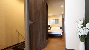 A hotel room with a wooden floor, a bed with a white headboard, a window with blinds, and a white vase with flowers. - Elizabeth Garden Kuromon (Osaka)