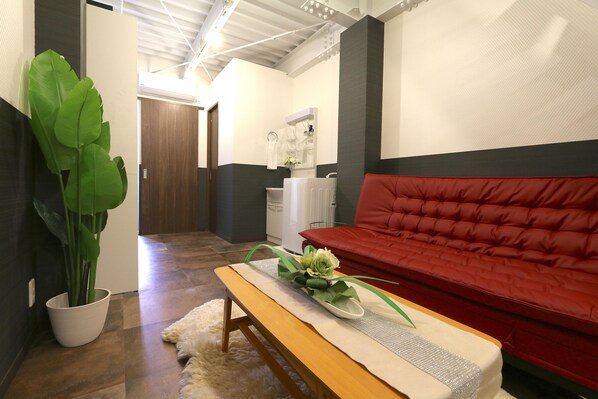 A modern living room with a red sofa, a wooden bench, a potted plant, and a white radiator. - Elizabeth Garden Kuromon (Osaka)
