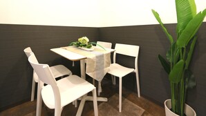 A corner dining area with white chairs and a table, a potted plant, and a dark-colored wall. - Elizabeth Garden Kuromon (Osaka)
