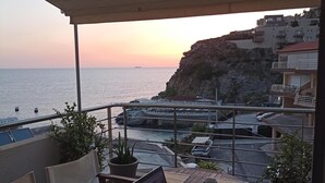 En balkon med en bærbar computer, en rød mus og en kop på et træbord. I baggrunden ses vand og bygninger.