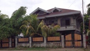 Une maison à deux étages dotée d’un balcon, entourée d’une clôture en bois et de palmiers.