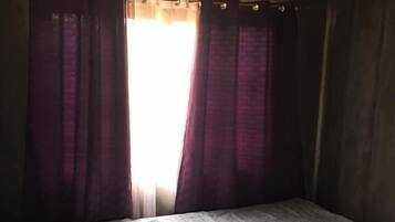 A room with a bed, purple curtains, and a window with sunlight.