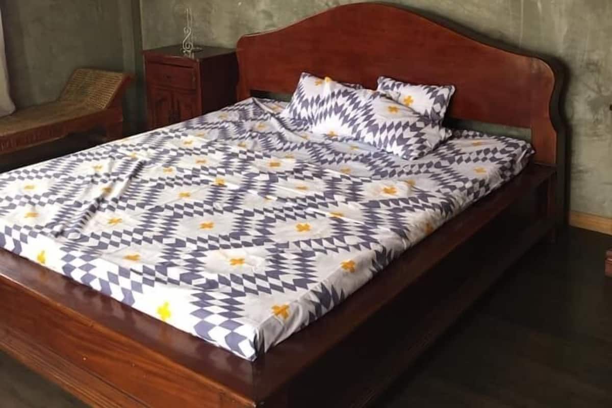 Un dormitorio con cabecera de cama de madera, colcha estampada, un reloj en la pared y una mesita de noche pequeña.