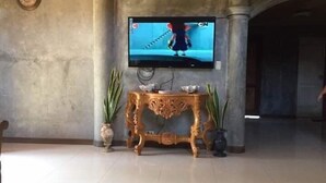 Un téléviseur fixé au mur, avec un meuble décoratif en dessous, et de part et d’autre, des plantes en pot.