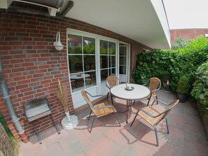 Une terrasse avec une table ronde et quatre chaises en osier, un mur en briques et une grande fenêtre.