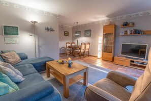 Un salon comprenant un canapé, une table basse, un téléviseur et un coin repas avec des chaises et une table.