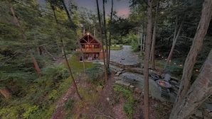 Une cabane entourée de forêt, dotée d’une terrasse en pierre et d’un foyer extérieur.