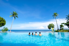Una piscina con cuatro personas nadando, rodeada de palmeras y vista al océano.