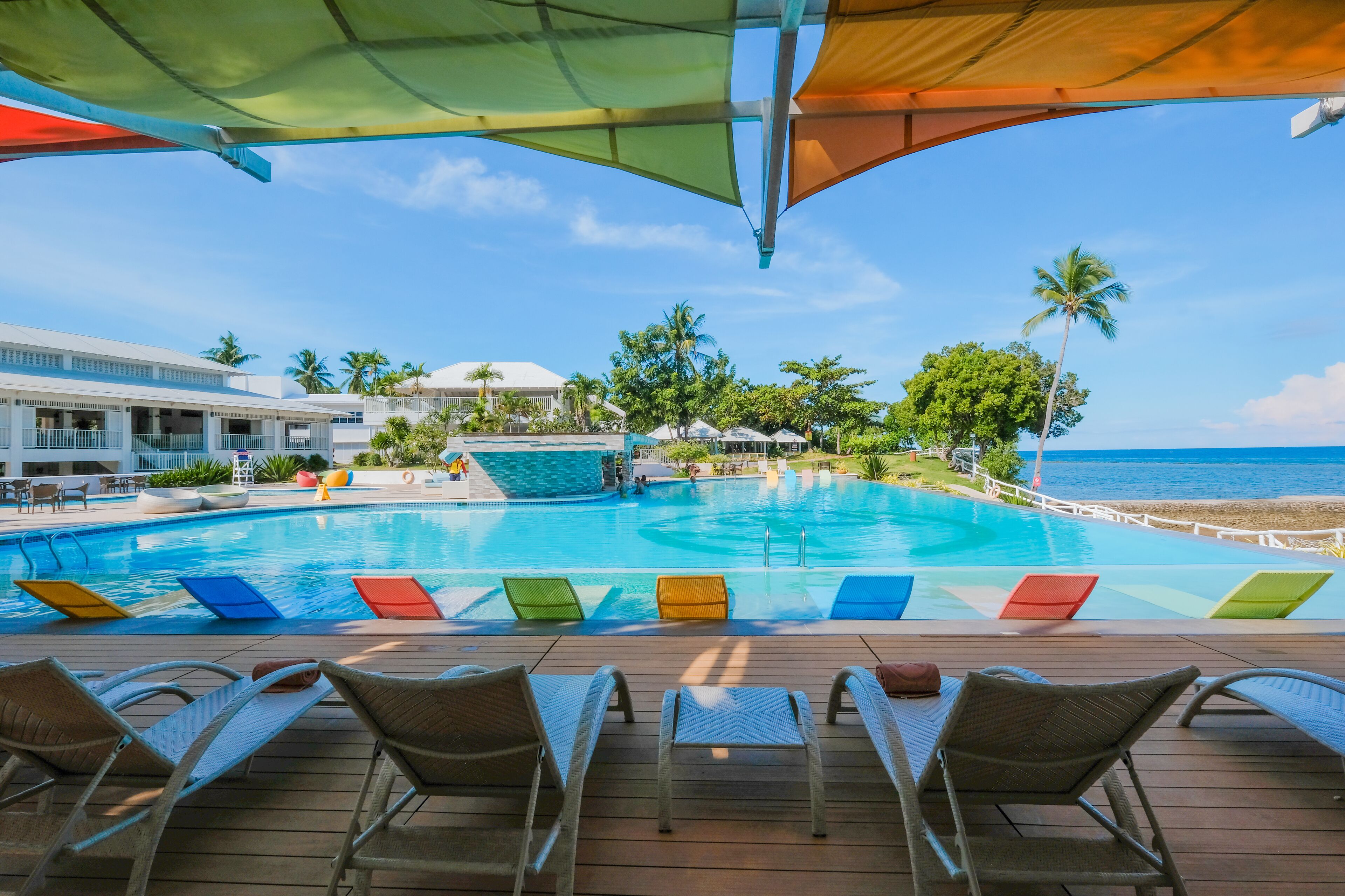 A poolside view with lounge chairs, a pool, and a view of the ocean.