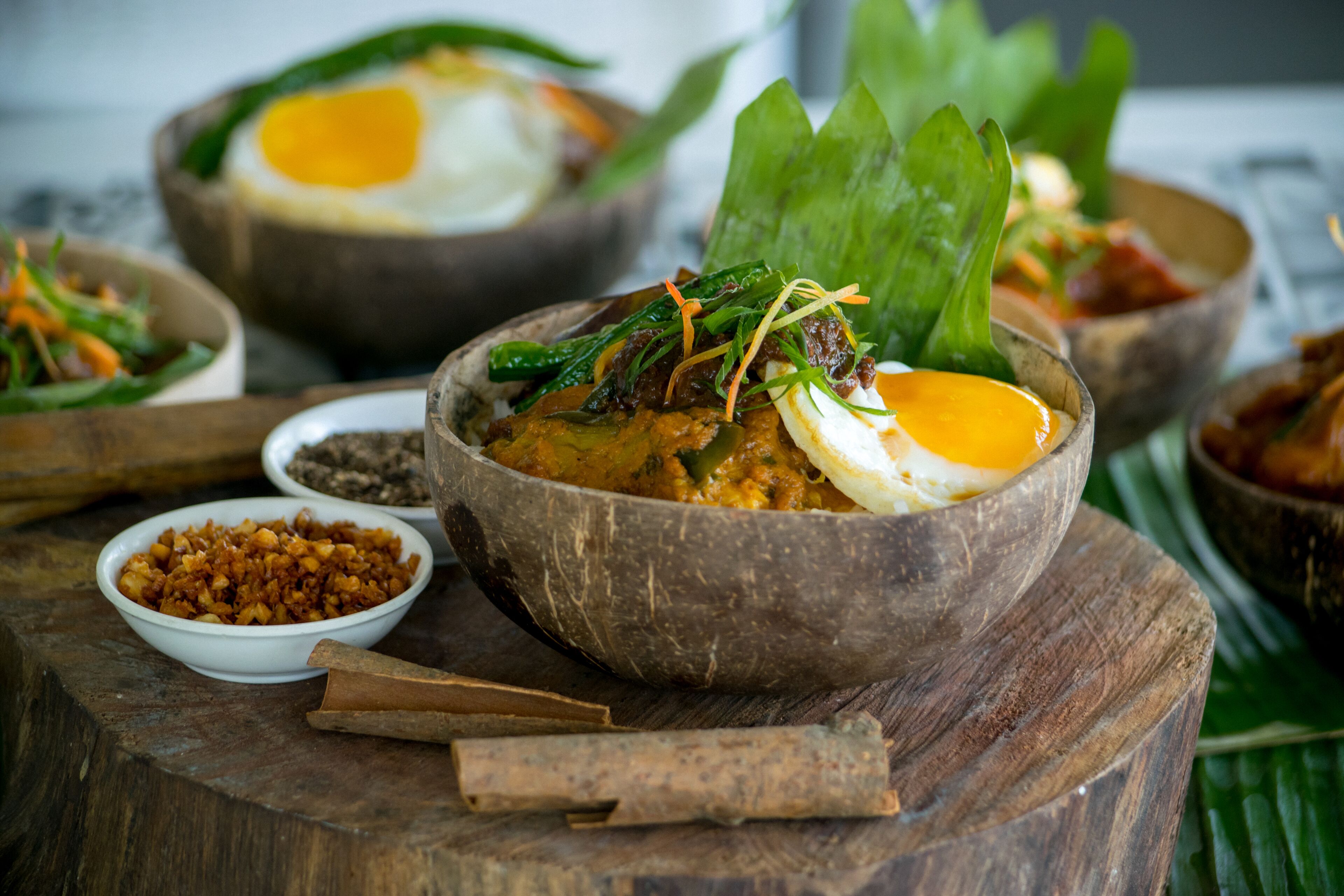 A wooden table with bowls of food, including a dish with a fried egg and greens, and a bowl of what appears to be a grain dish.