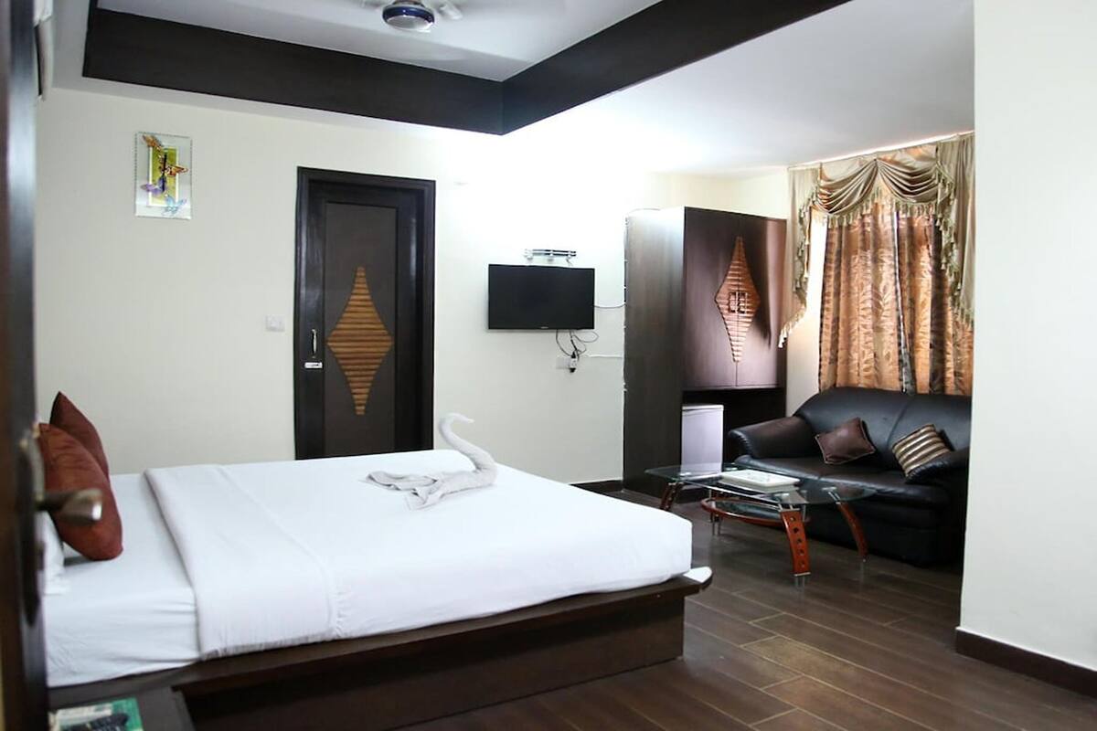 A hotel room with a bed, a TV, a sofa, and curtains.