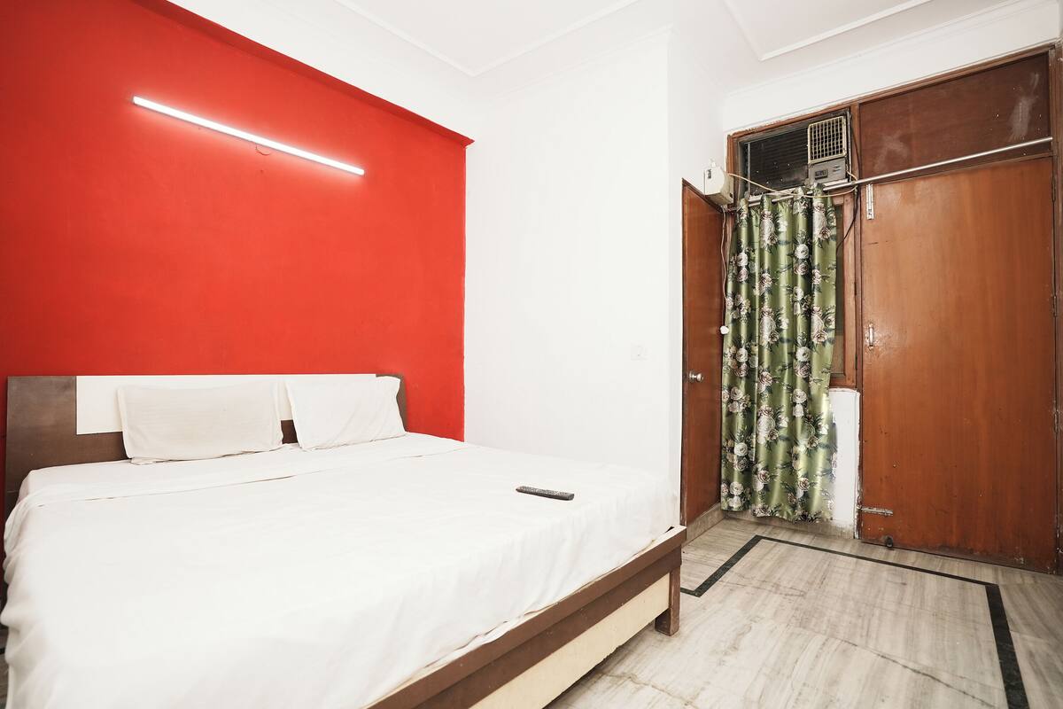 A bedroom with a bed, a red wall, a wooden wardrobe, and a curtain.