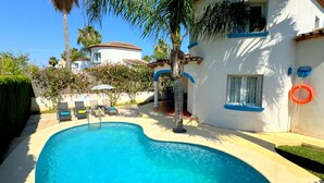 A swimming pool with lounge chairs, a palm tree, and a white building with blue trim. - 0676 Villa Molins Tauro (Denia)