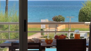 A balcony with a view of the sea, a table with fruits and a glass of juice, and a chair.