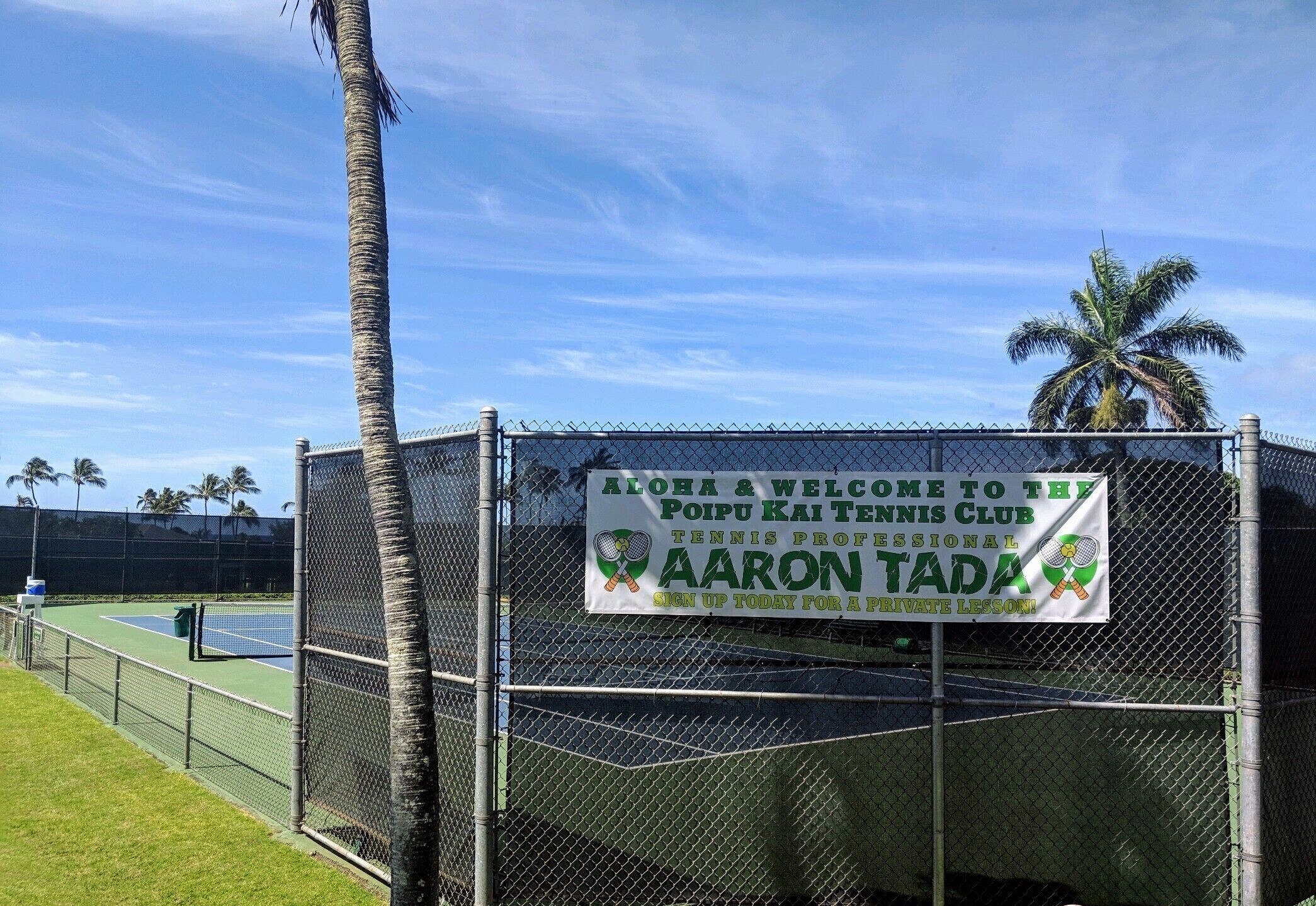 Una cancha de tenis con un cartel que anuncia una clase particular impartida por Aaron Tada.