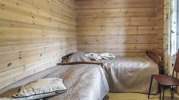 Quarto de cabana de madeira com duas camas, uma cadeira e janela com cortinas.