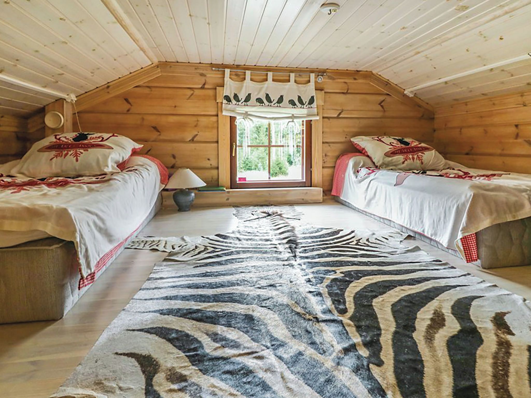 Een gezellig kamer in een blokhut met twee bedden, een vloerkleed met luipaardprint en een raam met gordijnen.