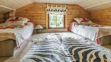 Een gezellig kamer in een blokhut met twee bedden, een vloerkleed met luipaardprint en een raam met gordijnen.