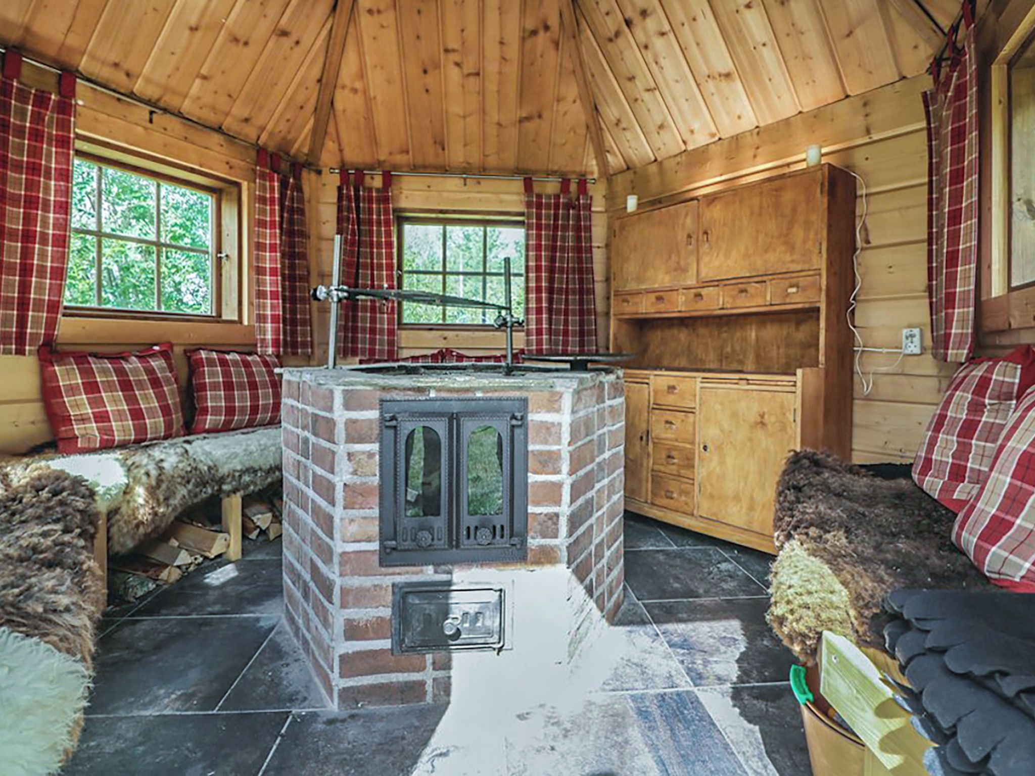 Un intérieur de chalet chaleureux avec une cheminée centrale, des murs en bois et des rideaux à carreaux.