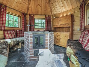 A cozy cabin interior with a central fireplace, wooden walls, and plaid curtains. - Ruuhikari by Interhome (Ulvila)