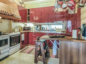 A kitchen with red cabinets, a wooden island, a stove, and various kitchen utensils. - Ruuhikari by Interhome (Ulvila)