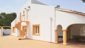Un edificio blanco con un patio empedrado, una escalera y una zona de estar cubierta al aire libre.